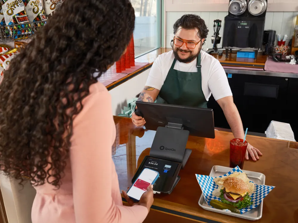 Dono de lanchonete atende cliente que paga por aproximação com o celular, representando o microempreendedor individual