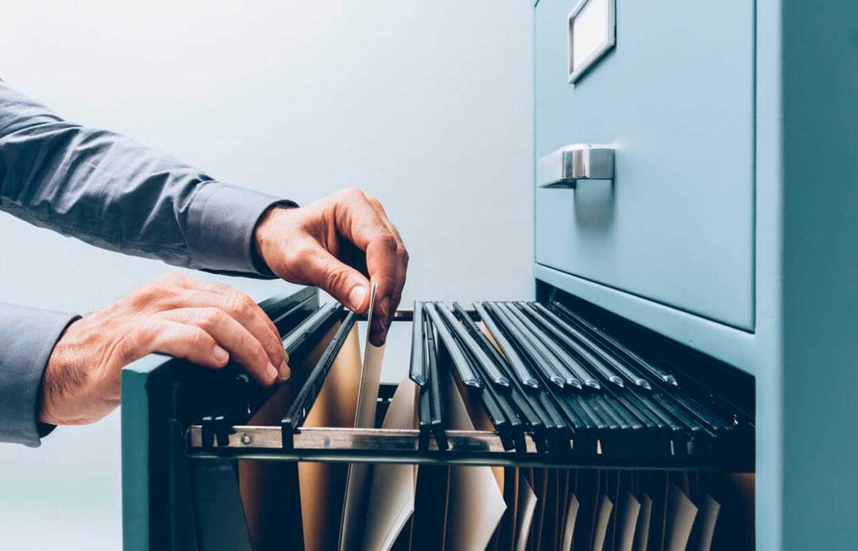 Pastas de documentos ao lado de um notebook digitalizando papéis, ilustrando o prazo de guarda de documentos da empresa