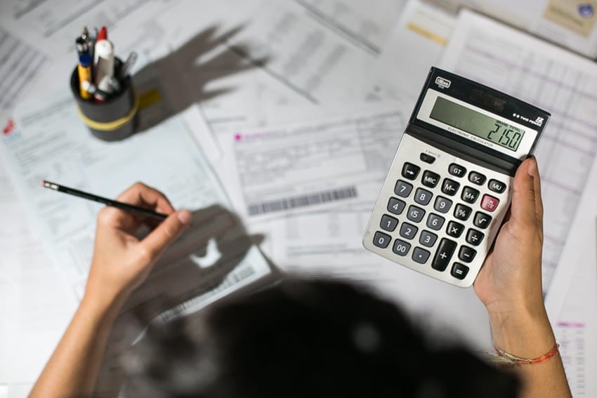 Pessoa usando calculadora sobre guias e documentos, representando o cálculo de quanto o MEI paga por mês
